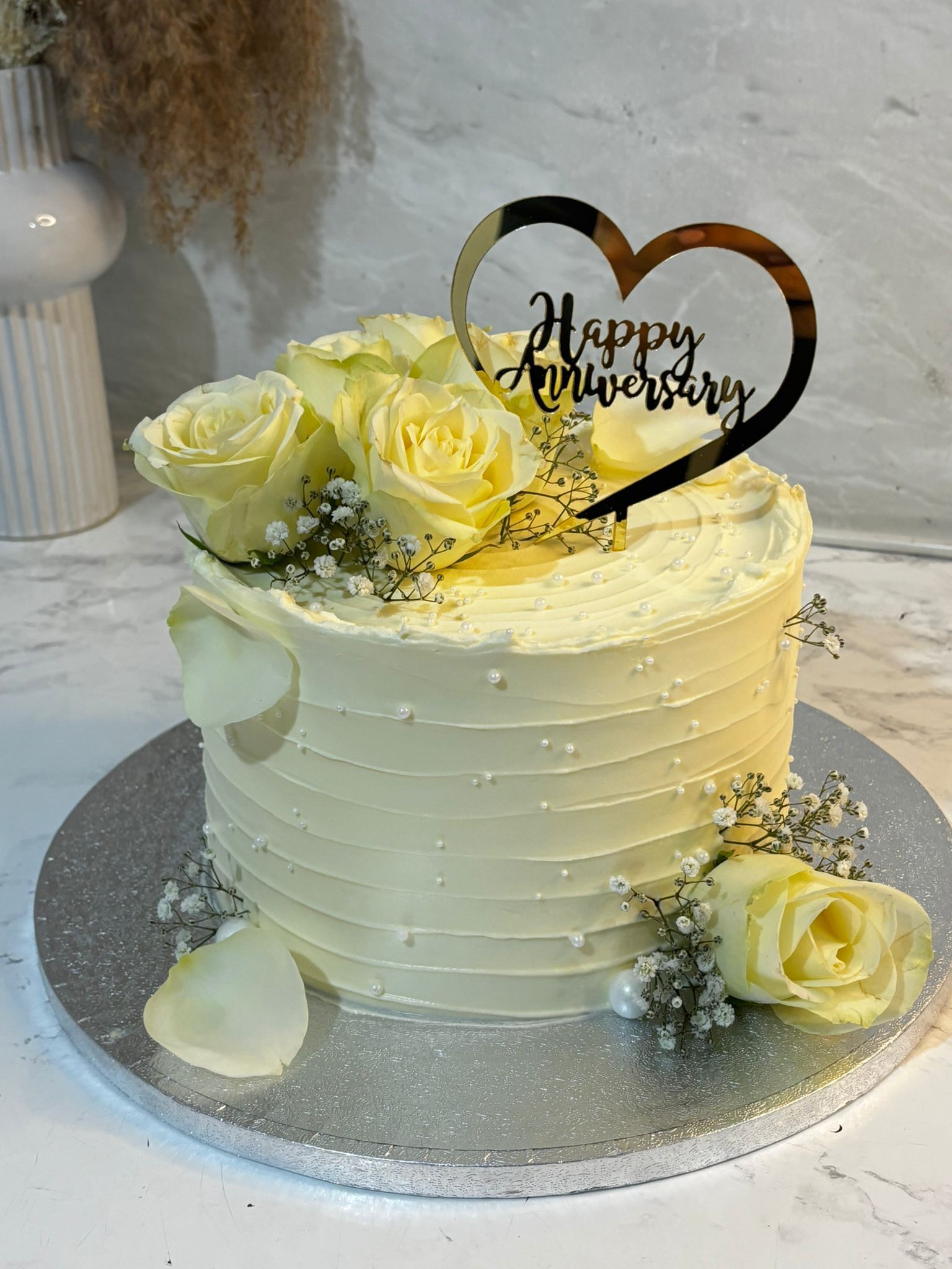 Anniversary cake decorated with ivory roses and heart topper