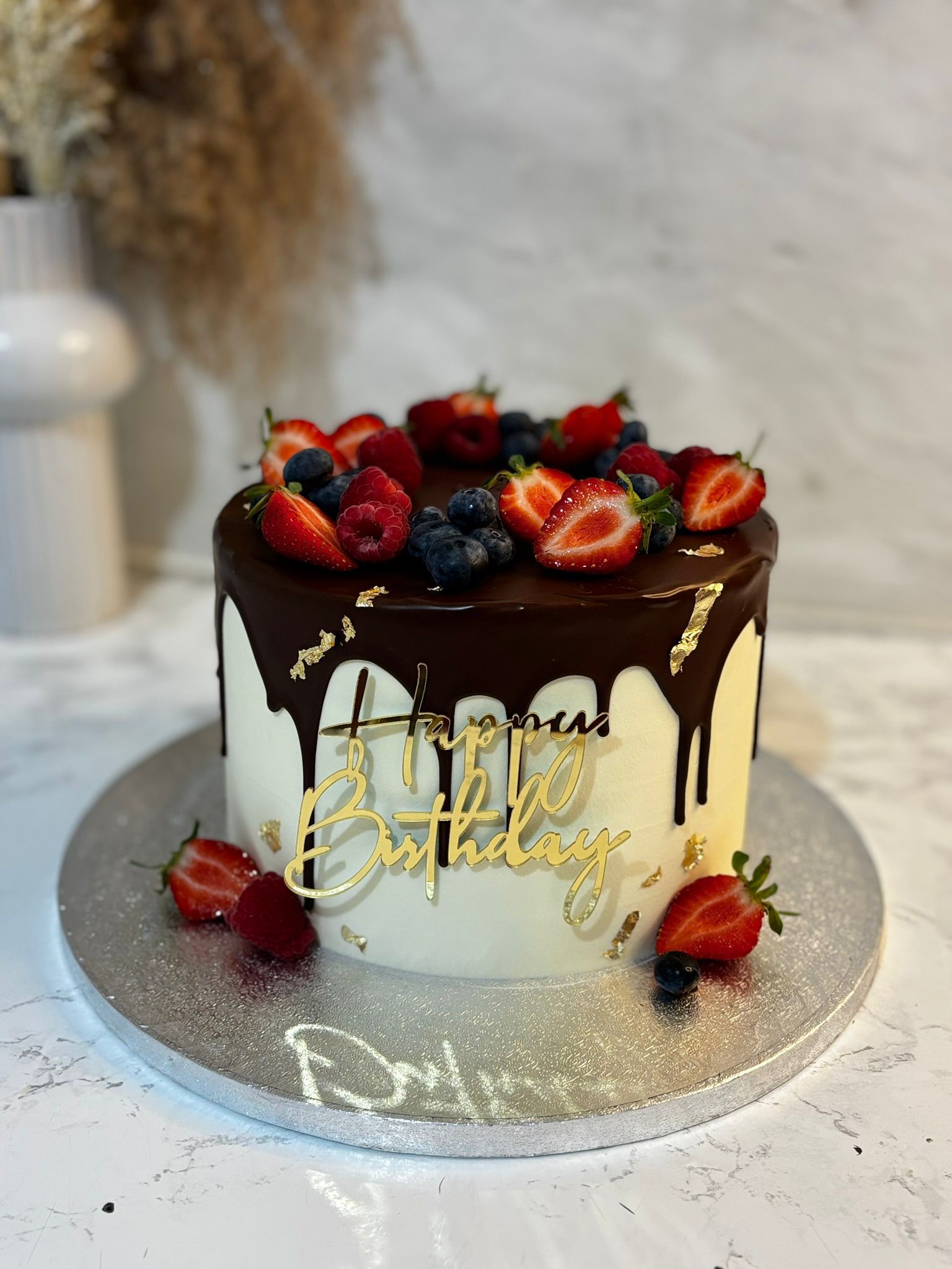 Chocolate drip cake topped with mixed berries and gold accents