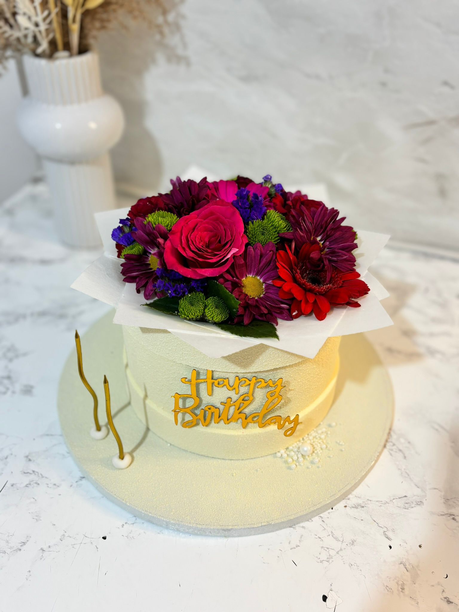 Cake topped with a colourful bouquet arrangement and birthday text