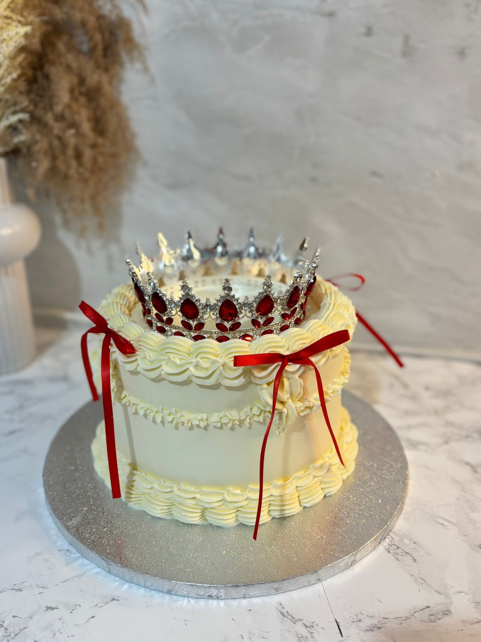 White cake with red crown topper and red ribbon accents