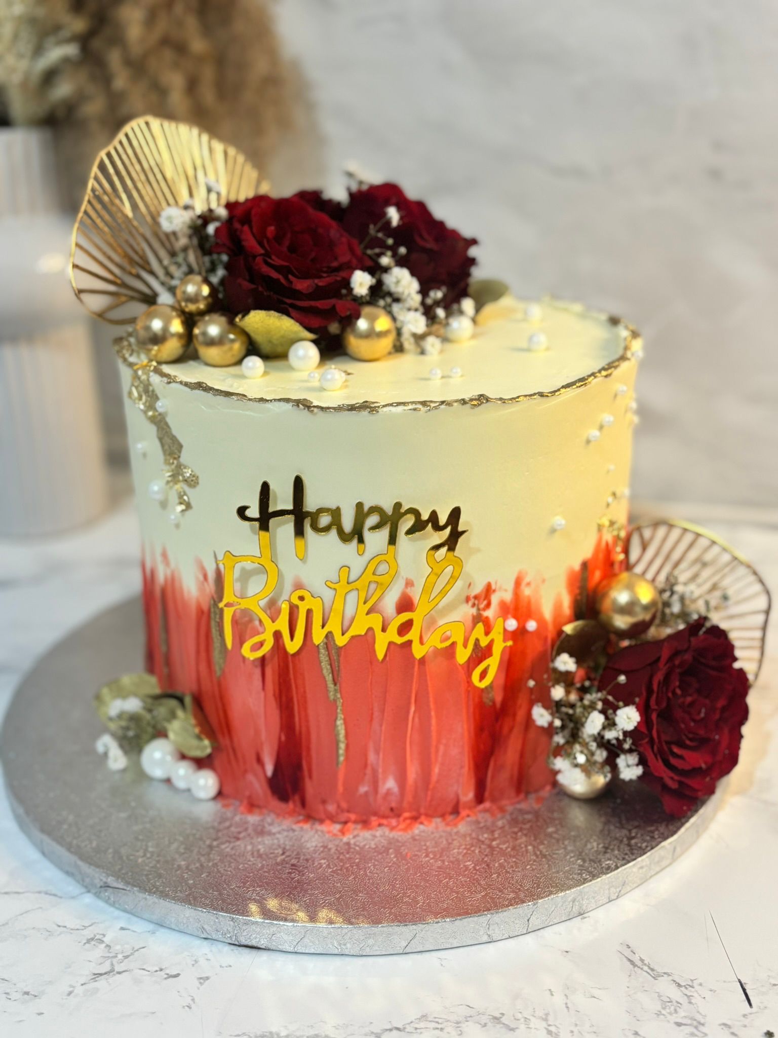 Modern cake with red floral accents, gold details and birthday topper